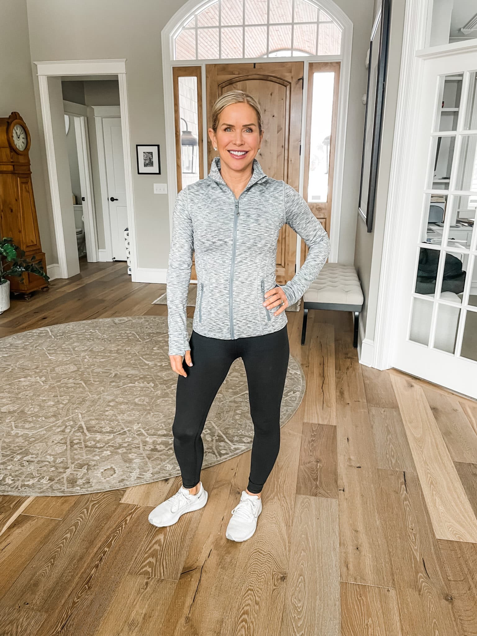 Chris Freytag wearing a full zip grey jacket with black leggings. Posing in the front entry way.