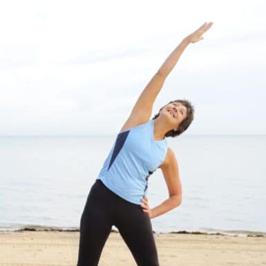 woman standing on beach in workout clothes doing a standing side bend